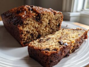 Close-up of a loaf of moist vegan banana bread, partially sliced, showing chocolate chips throughout the crumb.