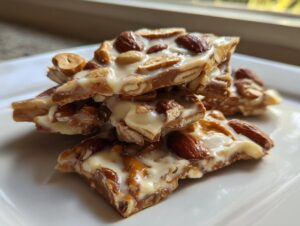 A stack of broken pieces of homemade peanut butter pretzel bark topped with almonds and white chocolate.