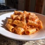 A close-up shot of rigatoni pasta coated in creamy pink sauce pasta, seasoned with black pepper, served in a white bowl.