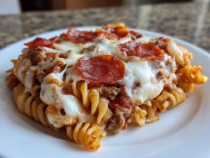 A close-up serving of pizza pasta bake featuring rotini pasta, meat sauce, melted mozzarella, and pepperoni slices.