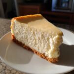 A thick, creamy slice of Protein Cheesecake with a golden graham cracker crust, sitting on a white plate.