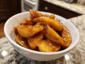 Close-up of glossy, cinnamon-spiced apple pie filling slices served in a small white bowl.