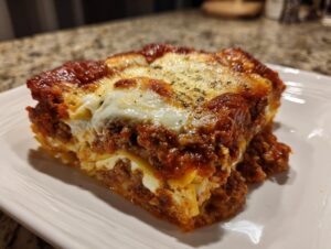 Close-up of a baked slice of ravioli lasagna with rich meat sauce and melted cheese topping.