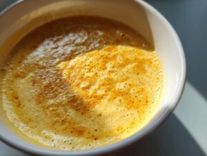 Close-up of a steaming bowl of vibrant yellow cheese soup with a frothy top layer.