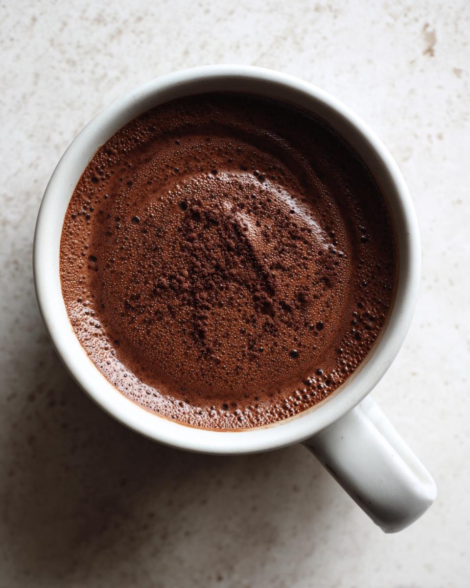 Overhead view of thick, rich chocolate pudding topped with cocoa powder in a white mug.