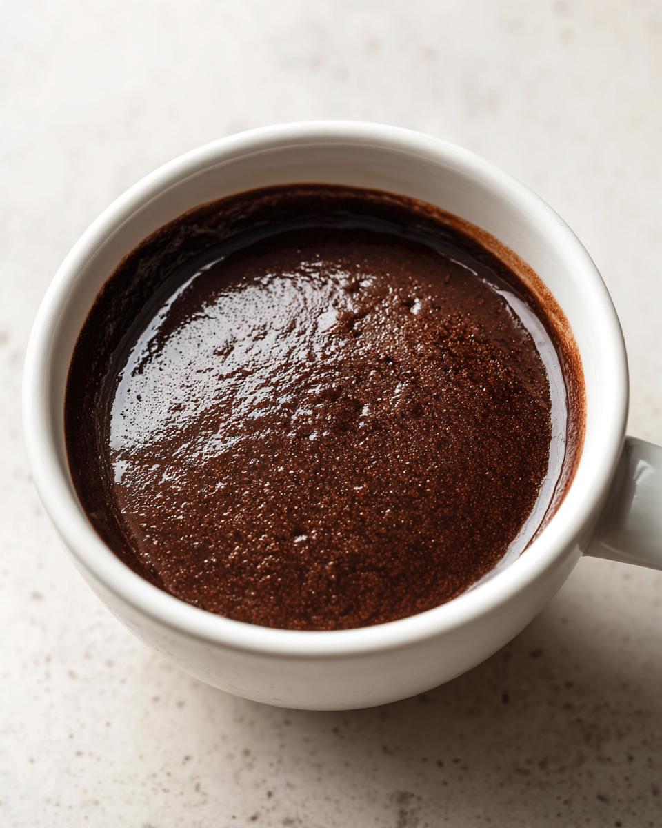 Close-up of rich, dark chocolate pudding with a slightly glossy surface in a white mug.