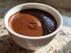 Close-up of rich, dark chocolate pudding with a slight froth texture in a white bowl.