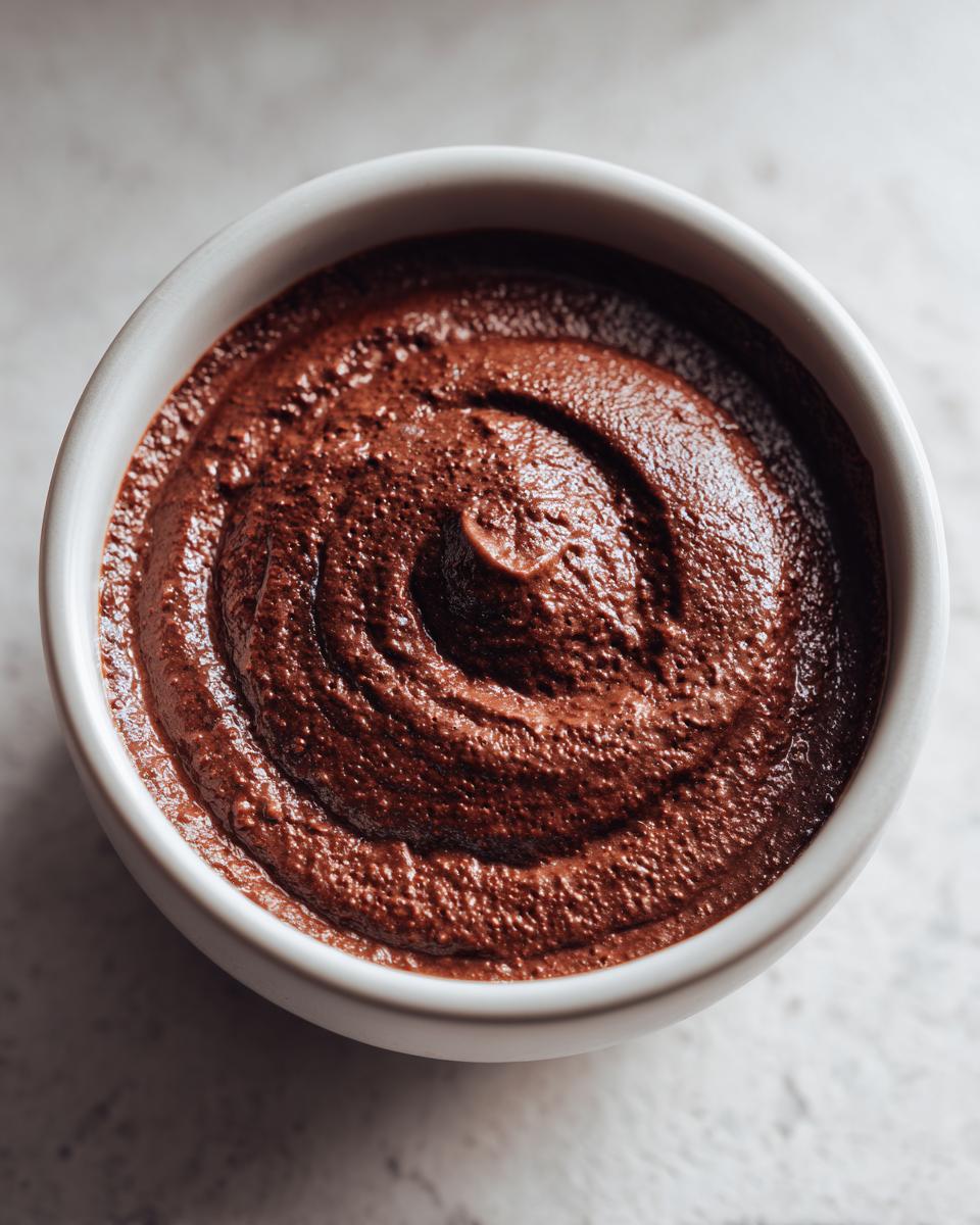 Overhead close-up of thick, rich chocolate pudding with a distinct swirl pattern in a small white bowl.