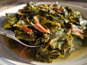 A close-up of a fork lifting savory collard greens cooked with pieces of smoked ham hock.