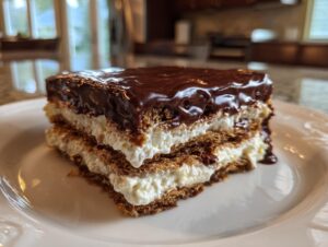 A close-up of a layered slice of chocolate eclair cake with creamy filling and glossy chocolate topping.