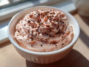 Close-up of creamy pink smoked salmon dip topped with cracked black pepper in a white bowl.