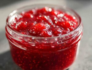 Close-up of bright red strawberry freezer jam with visible fruit pieces in a small glass jar.