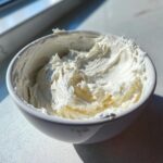 A white bowl filled with thick, fluffy, white royal icing recipe mixture, brightly lit by sunlight.