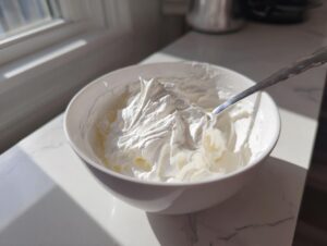 Thick, bright white royal icing recipe mixture whipped in a white bowl with a spoon resting inside.