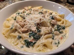 A close-up of a white bowl filled with creamy white chicken lasagna soup, featuring pasta, shredded chicken, spinach, and grated Parmesan.