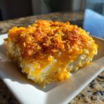 A close-up, sunlit serving of creamy potato casserole topped with crispy, golden cornflakes and black pepper.