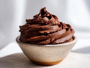 A close-up of rich, dark chocolate frosting piped high in a speckled ceramic bowl.
