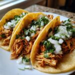 Three soft corn tortillas filled with shredded, seasoned chicken, topped with diced white onion and fresh cilantro for amazing chicken tacos.
