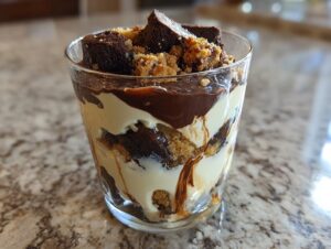 Close-up of a single serving Baileys Chocolate Cheesecake Trifle layered with cream, chocolate sauce, and brownie pieces.