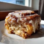 A close-up of a single, gooey cinnamon roll with thick white icing, highlighting the texture of the cinnamon rolls with heavy cream.