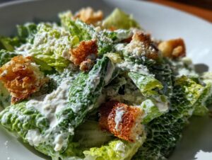 Close-up of a vibrant caesar salad featuring crisp romaine lettuce generously coated in creamy dressing and topped with golden croutons.