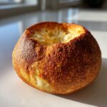 A single, perfectly round, golden-brown bread bowl with a hollowed-out center, ready for filling.