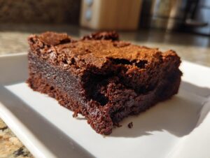 Close-up of a rich, fudgy slice of date brownies with a crackly top, sitting on a white plate.
