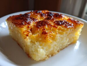 A square slice of moist cassava cake with a deeply caramelized, golden-brown top, resting on a white plate.