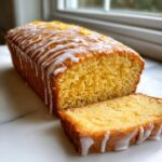 Close-up of a moist olive oil cake loaf, sliced, drizzled with white lemon glaze and orange zest.