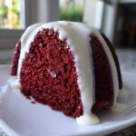 Close-up of a slice of moist red velvet bundt cake topped with thick white glaze dripping down the sides.