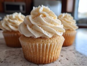 Close-up of a perfectly baked vanilla cupcake topped with swirled white vanilla frosting and white sprinkles.