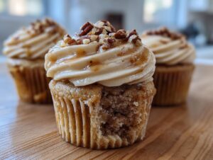 A close-up of a pecan pie cupcakes with a bite taken out, showing the moist interior and caramel frosting topped with chopped pecans.