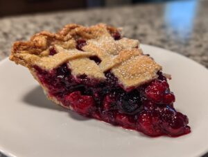 A close-up of one perfect slice of triple berry pie showing juicy berries and a sugared lattice crust.