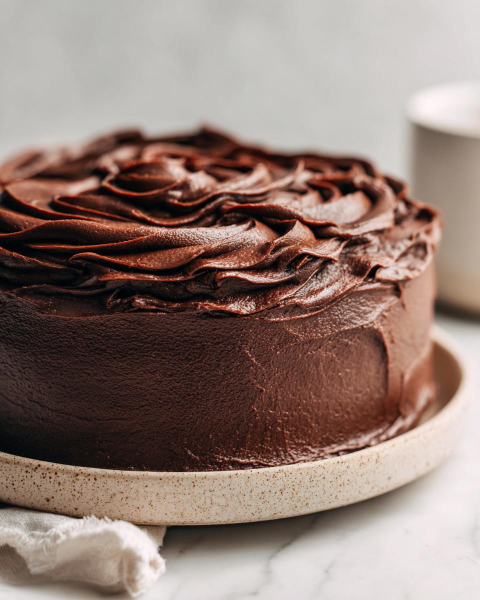 A decadent layer cake generously covered in rich, dark chocolate frosting with swirled peaks on top.
