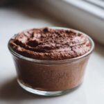 A close-up of rich, dark chocolate mousse topped with chocolate shavings in a small glass dish.