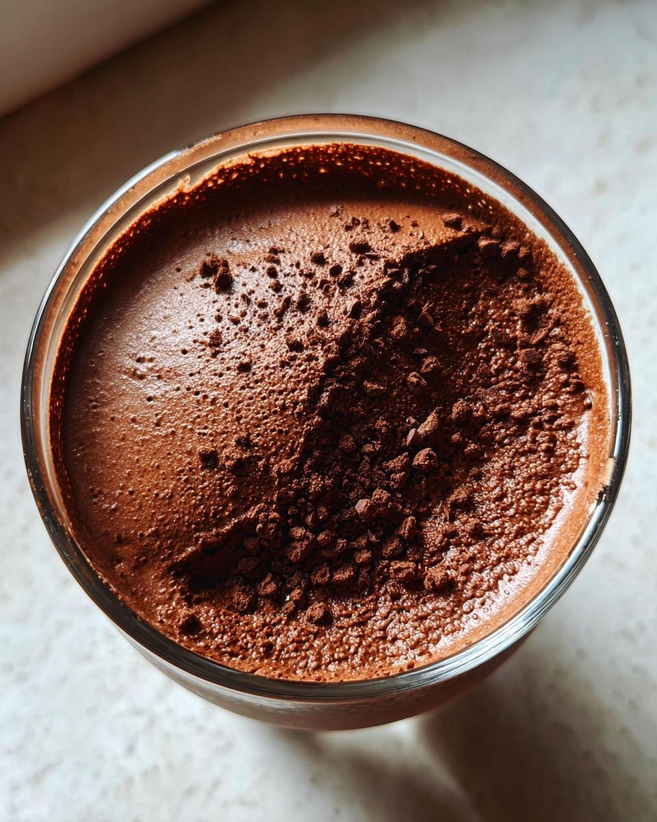 Overhead view of a glass filled with rich chocolate mousse, dusted heavily with cocoa powder.