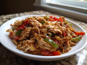 A close-up of shredded chicken mixed with sautéed onions and colorful bell peppers for crockpot chicken fajitas.
