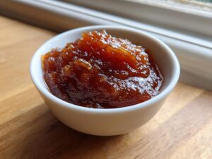 A close-up of rich, dark brown pear butter served in a small white bowl on a wooden surface.