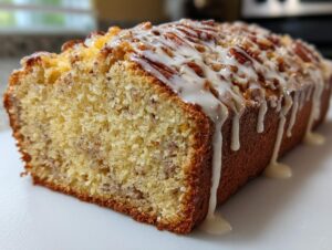 A close-up of a freshly baked loaf of sweet Alabama pecan bread, drizzled with a thick vanilla glaze and topped with pecans.