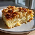A close-up of a rich, creamy slice of squash casserole with a thick, browned crumble topping.