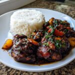 A plate featuring rich brown stew chicken next to a mound of fluffy white rice.