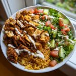 Close-up of a chicken shawarma crispy rice salad bowl with seasoned chicken, yellow rice, fresh salad, and white sauce drizzle.