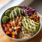 A vibrant vegan buddha bowl featuring quinoa, roasted sweet potatoes, broccoli, avocado, and tahini dressing.