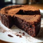 A rich, dense slice cut from a flourless chocolate cake dusted heavily with cocoa powder.