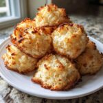 A pile of freshly baked, golden brown coconut macaroons with toasted edges on a white plate.
