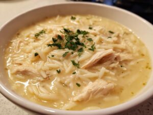 Close-up of a creamy bowl of greek lemon chicken orzo soup, garnished with fresh parsley.