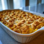 A freshly baked squash casserole with ritz crackers topping in a white baking dish.