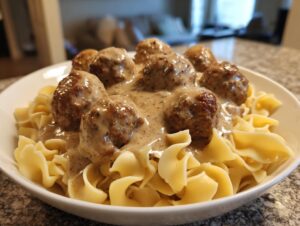 A white bowl filled with tender Swedish meatballs smothered in creamy gravy served over wide egg noodles.