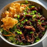 Close-up of a teriyaki chicken crispy rice salad featuring glazed chicken, greens, and large crispy rice pieces.