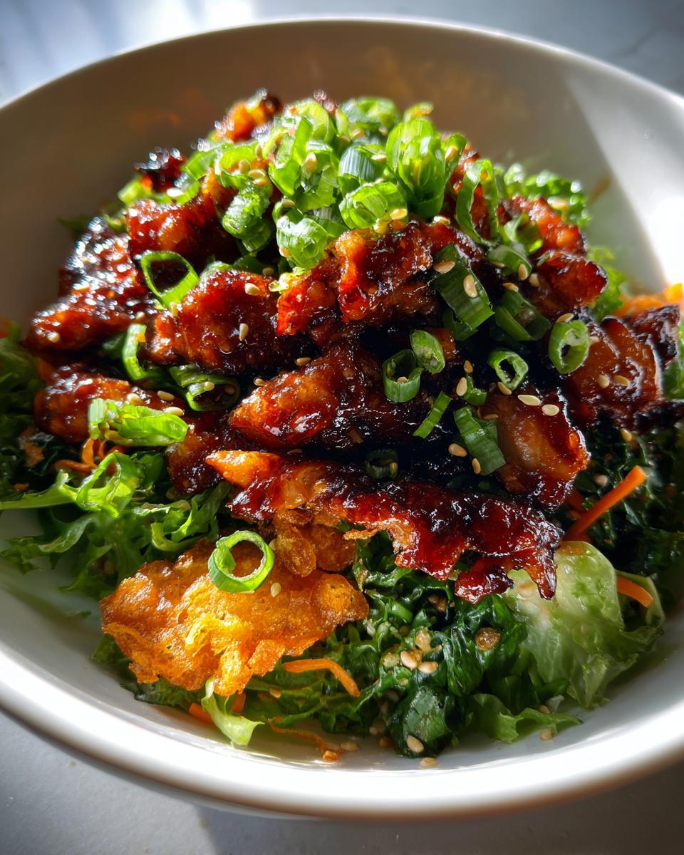 Close-up of teriyaki chicken crispy rice salad featuring glazed chicken, mixed greens, and scallions in a white bowl.